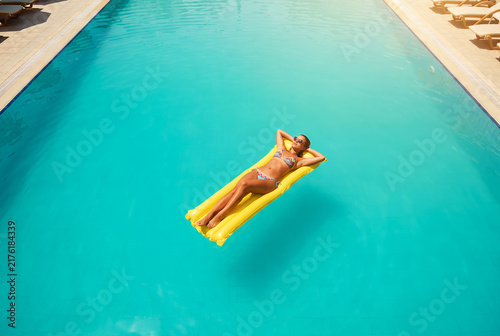 Woman floating on yellow pool float in turquoise swimming pool