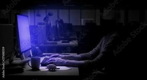 Heavy atmosphere at a workstation where dim lighting and a glowing monitor highlight quiet exhaustion during a late night office shift, screen, lamp, stillness