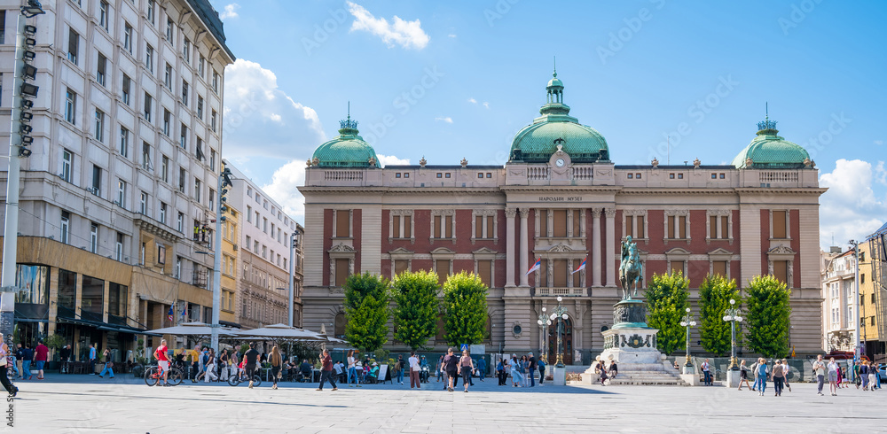 Obraz premium Belgrade National Museum with green domes and equestrian monument on Republic Square, surrounded by historic buildings, cafes, and visitors