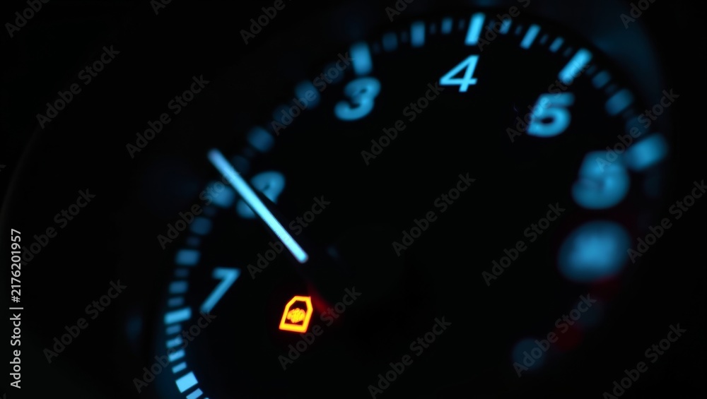Fototapeta premium Illuminated car dashboard with an active orange immobilizer warning light, showing speedometer and tachometer numbers in blue