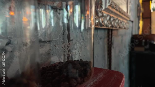 Handheld Close Up Dolly Tracking Shot Sliding Along Rows of Whole Dark Roasted Coffee Beans Stored in Glass Jars on Weathered Scratched Wooden Shelf inside Rustic Loft Cafe with Concrete Wall