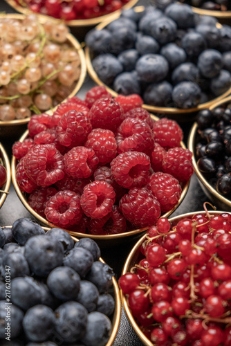 Fresh Raspberries In Focus Among Assorted Summer Berries In Bowls