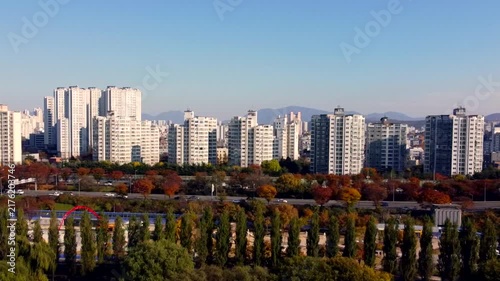 High rise apartment district overlooks autumn greenery, showing modern residential towers beyond colorful park trees. Urban development and fall foliage create vibrant metropolitan landscape