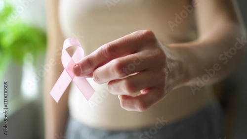 Close-up of female hand holding pink satin ribbon, symbolizing support for breast cancer awareness, medical care, and self-examination.
