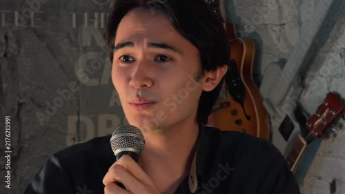 Emotional Asian Man Speaking Into Microphone On Empty Stage Conveying Power Of Words And Isolation Abstract Concept In Cozy Cafe Club With Warm Spotlight Close Up Handheld Documentary Lifestyle