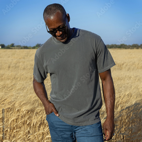 Blank washed grey t-shirt mockup on black man in wheat field at sunset, front view with copy space