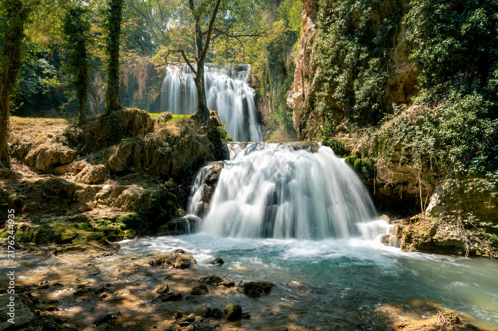 Obraz premium A silky waterfall flows over mossy travertine into an emerald pool in the Monasterio de Piedra natural park in Aragon Spain a serene and refreshing scene of water and lush greenery.