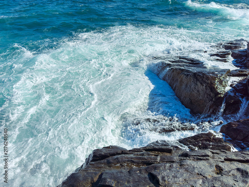 Photography Waves crash against rocks by the ocean during the day with sunlight and blue ski