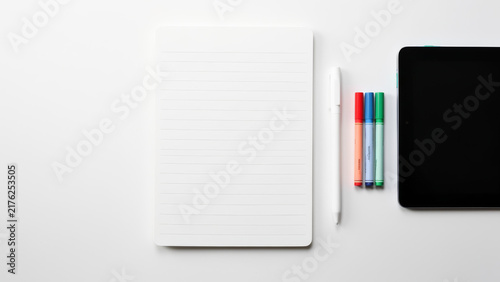 Minimal flat lay of blank notebook colorful pens and smartphone on a clean white desk providing a flexible planning writing study and creative workspace with generous copy space