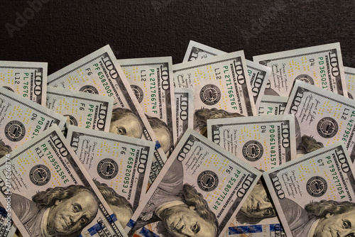 Scattered one hundred US dollar bills heap on dark background, closeup. High angle flat lay view of large pile of Benjamin Franklin 100 USD banknotes messy spread across black textured surface