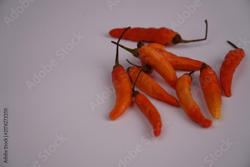 Fotografía Bright orange chilies are scattered over a plain white surface.