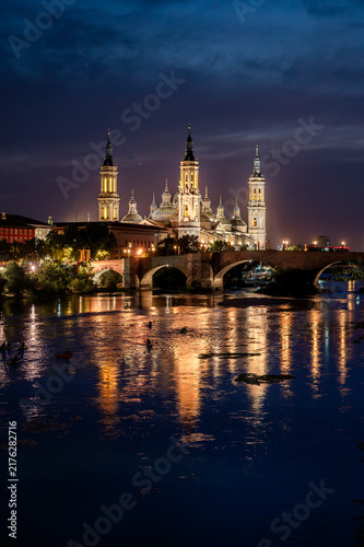 Картината върху платно The towers and domes of the Basilica del Pilar glow above the Ebro river and the Puente de Piedra at twilight in Zaragoza Spain a scenic vertical view of the iconic Spanish landmark at night