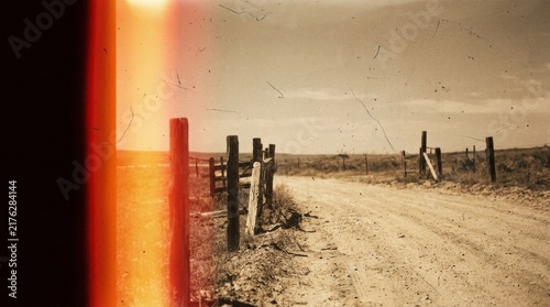 Dusty rural dirt road with wooden fence posts and vintage orange light leak