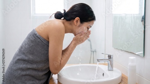 Young Asian woman washing face with foam cleanser at bathroom sink beauty skin care