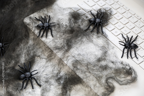 Hands working on a laptop surrounded by black spiders and cobweb decorations, creating a spooky Halloween atmosphere and concept of fear, digital threats and working from home.