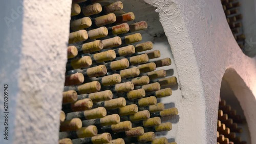 Old dusty wine bottles aging in a cellar. Numerous old, dusty wine bottles aging peacefully in a traditional stone cellar, showcasing the art of winemaking