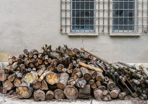 Haufen gelagerter Holzschete und Baumstämme, die lose vor einer verputzten mit vergittertem Fenster aufgeschichtet sind, Brandenburg, Deutschland