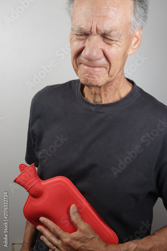 Older Man Applying a Hot Water Bottle on his stomach for pain relief  