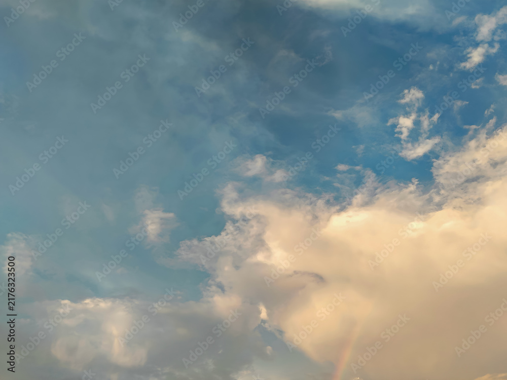 Fototapeta premium Beautiful blue sky with golden sunlight clouds and a subtle rainbow hint looking peaceful and dramatic at sunset time.