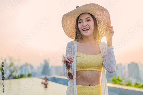 фотографія Portrait of cheerful smiling young woman wearing sun hat enjoying golden hour sunset at luxury rooftop, radiating joyful optimism, vitality, happiness, freedom, and vacation vibes