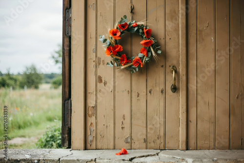 Poppy wreath hanging on weathered wooden door with field view during daytime