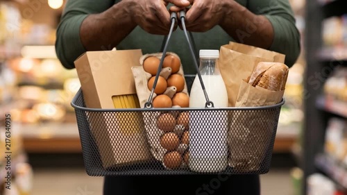 Close-up of a black male customer's hands holding a full grocery basket in front of them in a supermarket. Retail, daily food shopping and consumer lifestyle concept