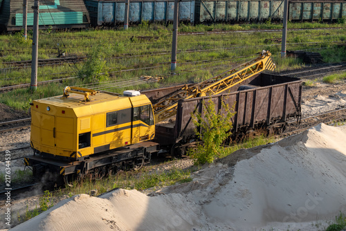 Cuadro en lienzo Yellow railway crane machine on tracks next to train cars