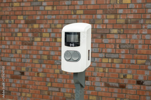 Fotografie Electric vehicle charging station mounted on a pole against a textured brick wal