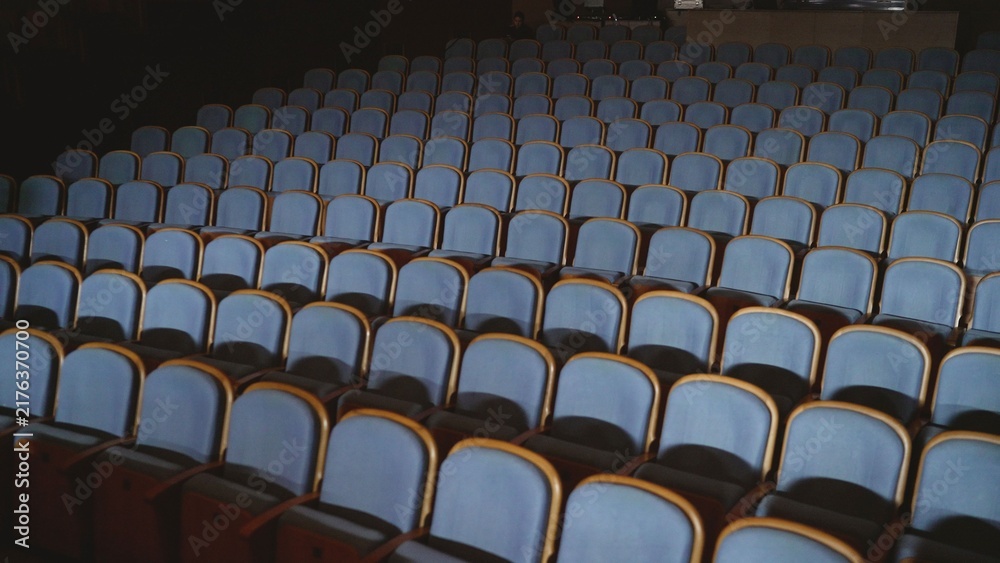 Fototapeta premium Rows of empty blue theater seats under dim lighting
