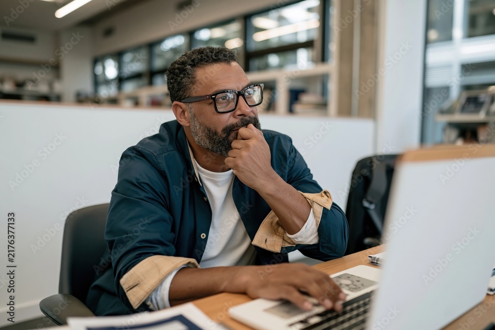 Obraz premium Businessman with deep skin tone thinking while using a laptop, natural and reflective in a bright office for business problem solving and focus