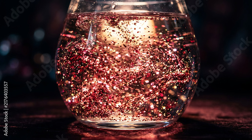 Glass bowl filled with swirling pink and red glitter in a dark room