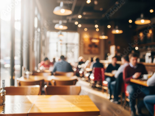 Blurred people sitting at wooden tables inside a cozy modern cafe restaurant