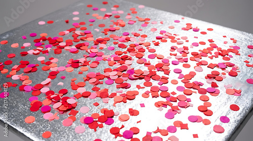 Red and pink confetti scattered on a textured silver surface