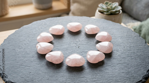 Rose quartz crystal hearts arranged in a circular formation on a rustic dark slate board