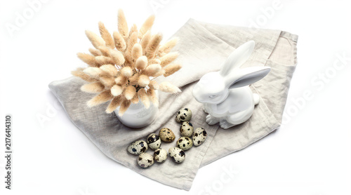 White ceramic rabbit and quail eggs with dried flowers on linen