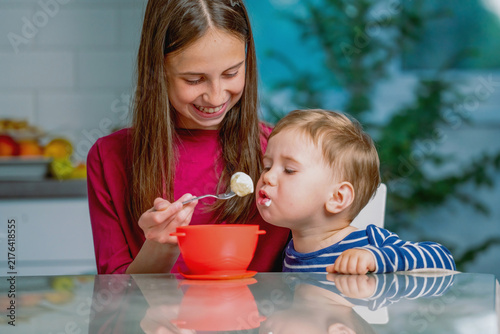 Older sister feeding her little brother with a spoon at home.