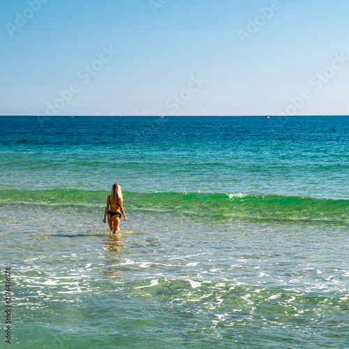 Woman walking into clear turquoise sea with wide horizon and copy space