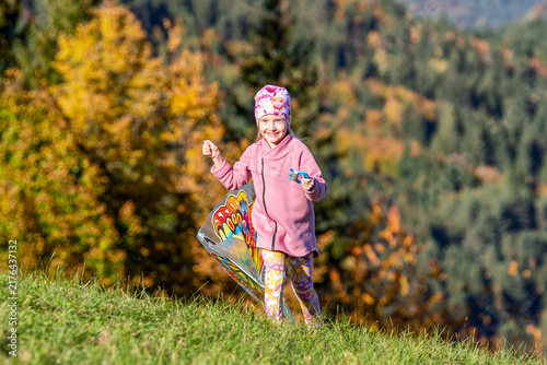 Happy child holding a kite in autumn nature with colorful forest background