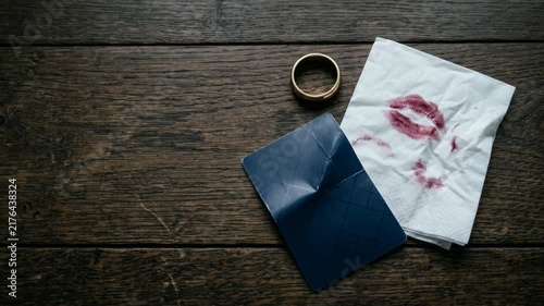 Wedding ring with lipstick stained napkin and credit card on wooden table. Broken marriage concept representing infidelity and relationship conflict between partners.