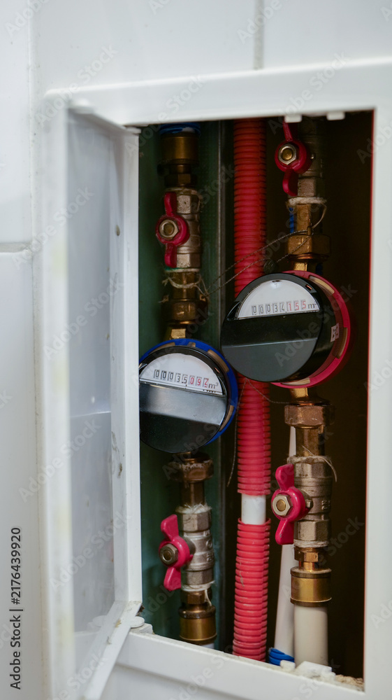Fototapeta premium Water meters and valves stationary, in indoor utility box, with water meter, valves, red hose, white cabinet, from a close-up perspective, with red, white accents, and neutral mood.