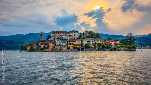Panoramic view of San Giulio Island on Lake Orta during a golden hour and sunset, Piedmont, Italy, featuring the historic basilica and picturesque lakeside scenery surrounded by Alpine landscapes