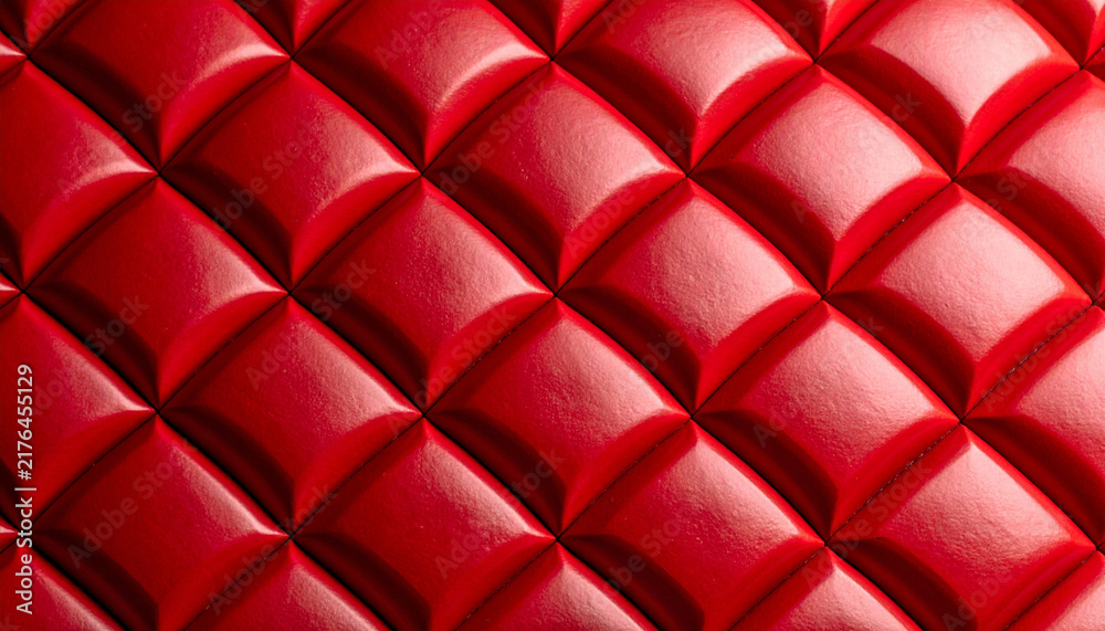 Obraz premium Close-up macro of a luxurious bright red quilted leather upholstery panel featuring a geometric diamond pattern and soft highlights. Interior design, background, and texture concept banner.