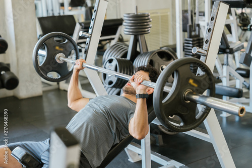 фотографія Determined man lifting heavy barbell weight bench press exercise in gym