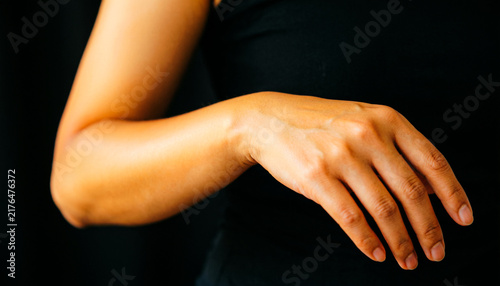 Elegant female hand and arm, graceful woman hand gesture on black background, soft skin texture and warm lighting