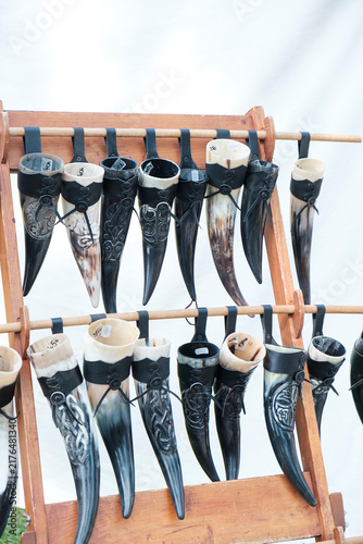 Fotografie Decorative traditional drinking horns displayed for sale on a wooden rack at a medieval or historical market, representing craftsmanship and reenactment culture