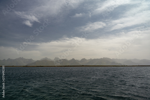 Calm Sea and Mountain Range on the Horizon With Coastal Strip Under Dramatic Cloudy Sky