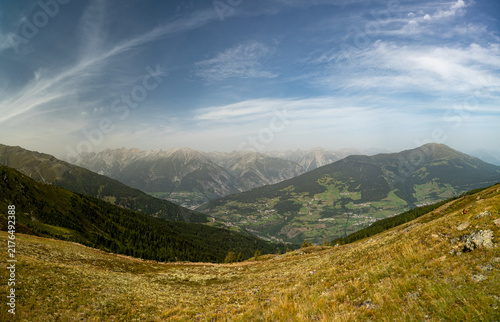 Panoramic Alpine Mountain Valley Landscape With Green Meadows, Forests and Distant Peaks Under Blue Sky