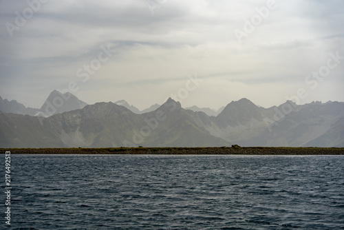 Calm Sea and Misty Mountain Range Beyond Rocky Coastal Shoreline Under Overcast Sky