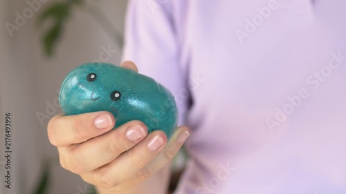 Hand pokes glossy teal squishy character toy closeup revealing soft deforming rubbery texture indoors calmly. Playful tactile press motion highlights collectible sensory toy for stress relief 