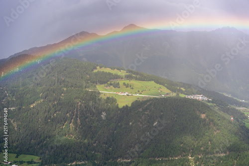 Vibrant Rainbow Arching Over Green Mountain Valley and Alpine Village Landscape